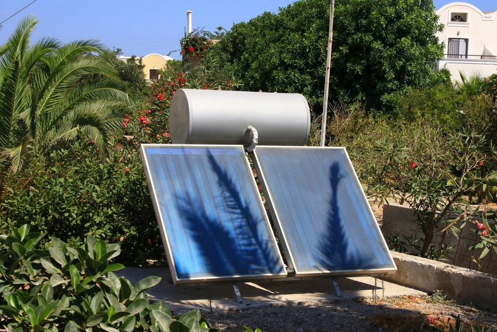 Système de chauffe-eau solaire installé dans un jardin résidentiel méditerranéen avec palmiers et végétation luxuriante