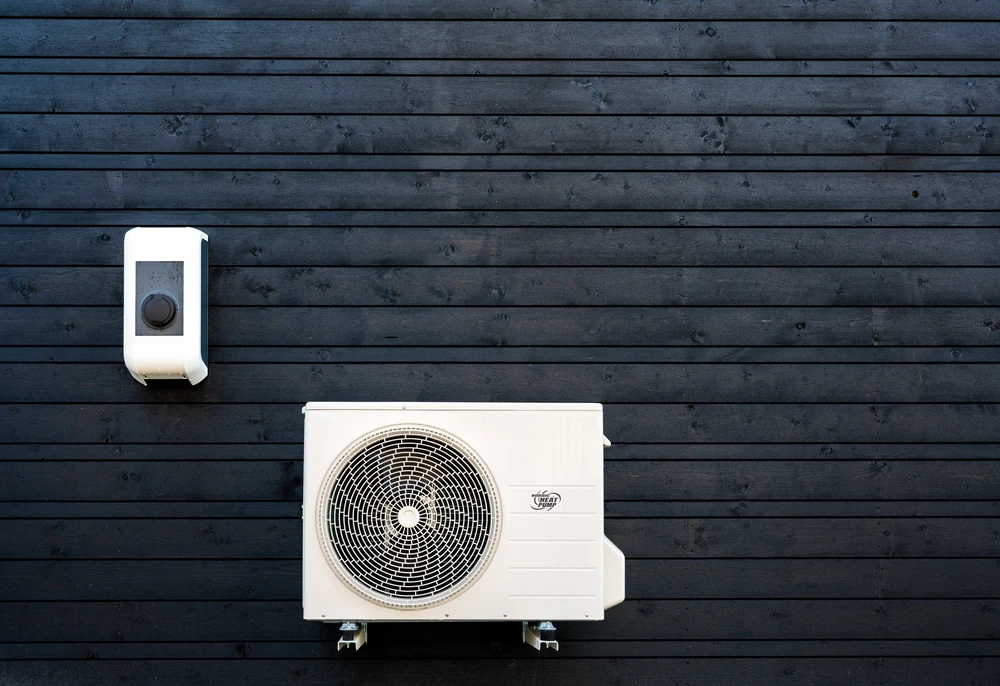 Façade extérieure en bardage bois foncé avec unité extérieure de climatisation split et boîtier de commande mural blanc