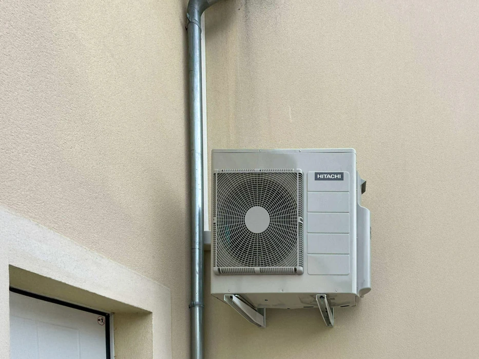 Extérieur d'une habitation avec unité extérieure de climatisation installée sur terrasse pavée, contre mur en pierre naturelle